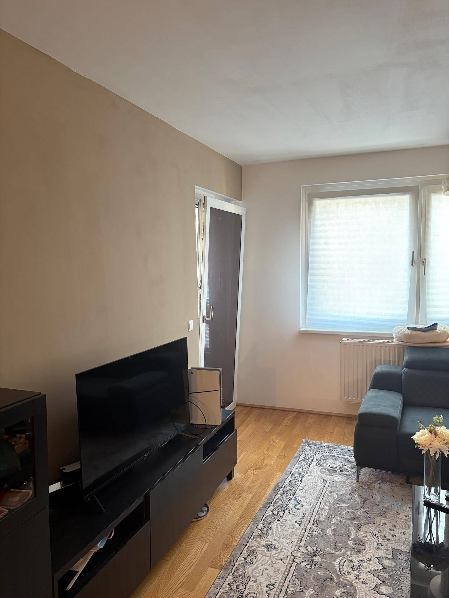 Wohnzimmer mit Fernseher auf einem Lowboard und Fenster mit Jalousien für Privatsphäre.