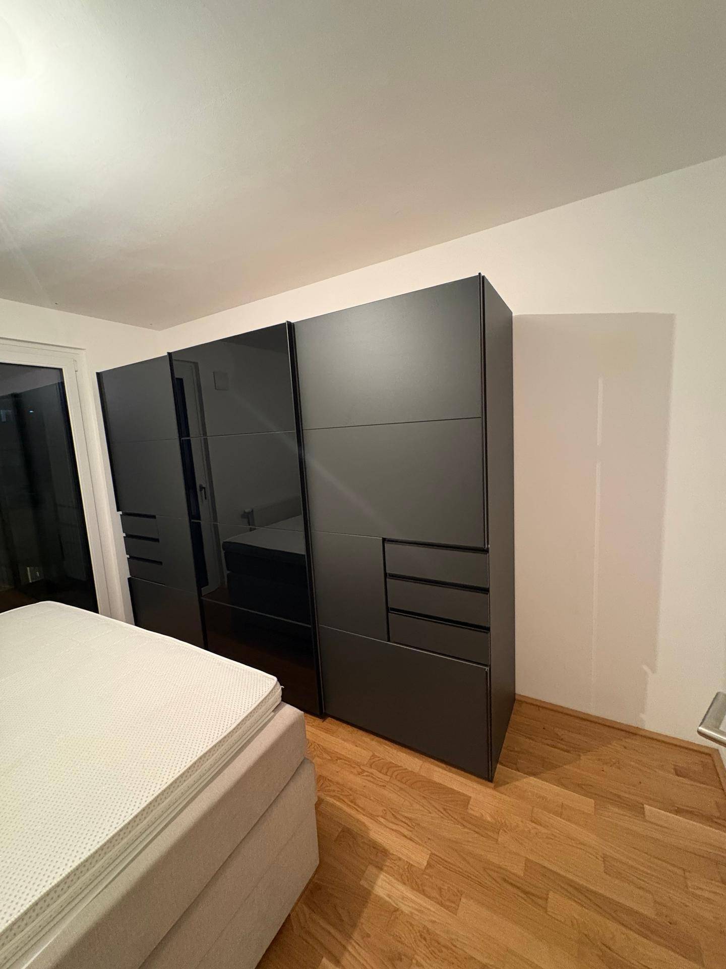 Schlafzimmer mit großem, modernem Kleiderschrank in dunklem Design und hellem Bett.