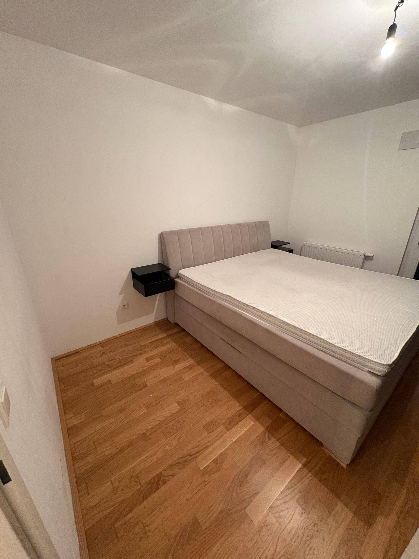Schlafzimmer mit hellem Boxspringbett, schwebenden Nachttischen und Holzfußboden.