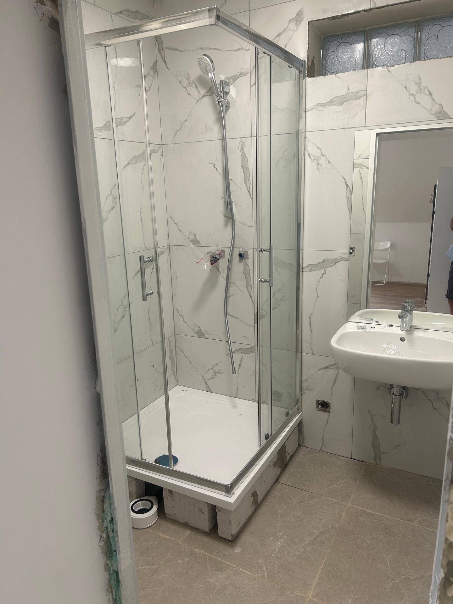 Modernes Badezimmer im Bau mit neuer Duschkabine, Waschbecken und hellen Fliesen.