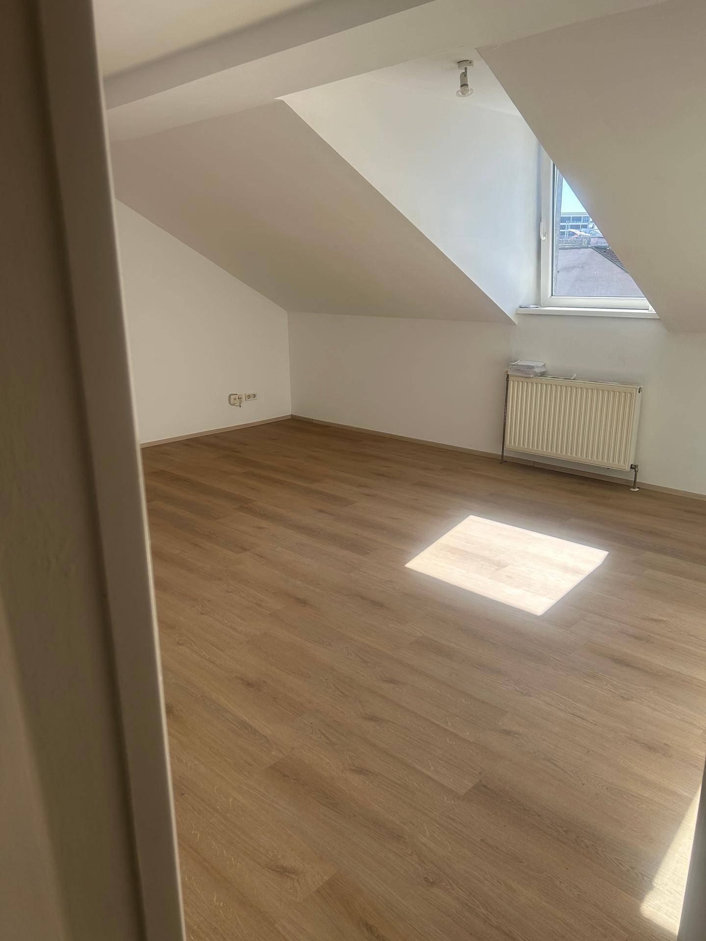 Geräumiges Zimmer im Dachgeschoss mit Laminatboden, Heizkörper und Fenster.