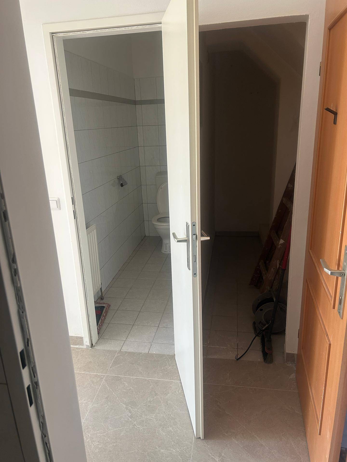 Separates WC mit Fliesenboden und Blick in einen angrenzenden Abstellraum.