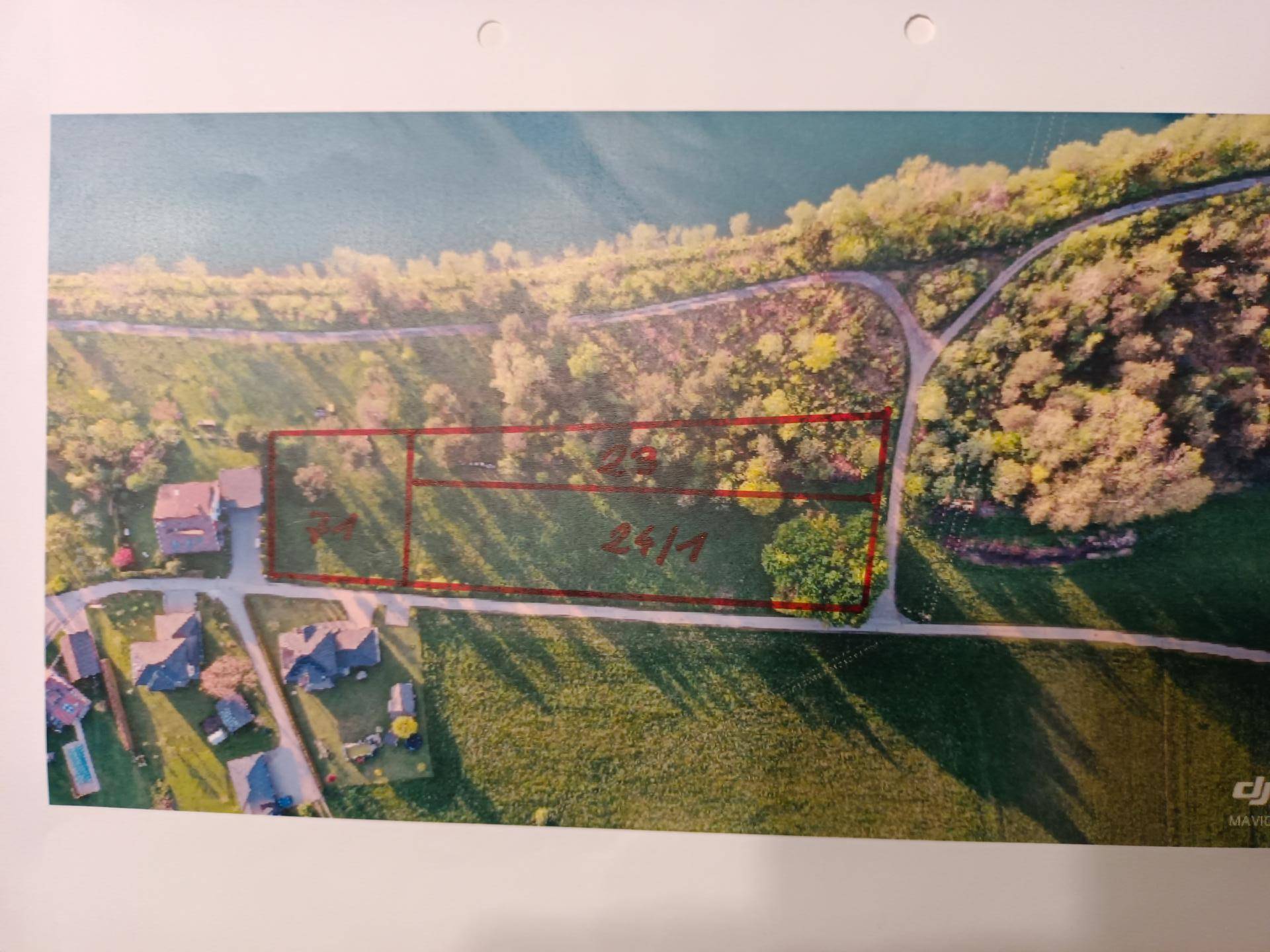 Luftbild mit rot markierten Grundstücksgrenzen und Parzellennummern entlang eines Flusses.