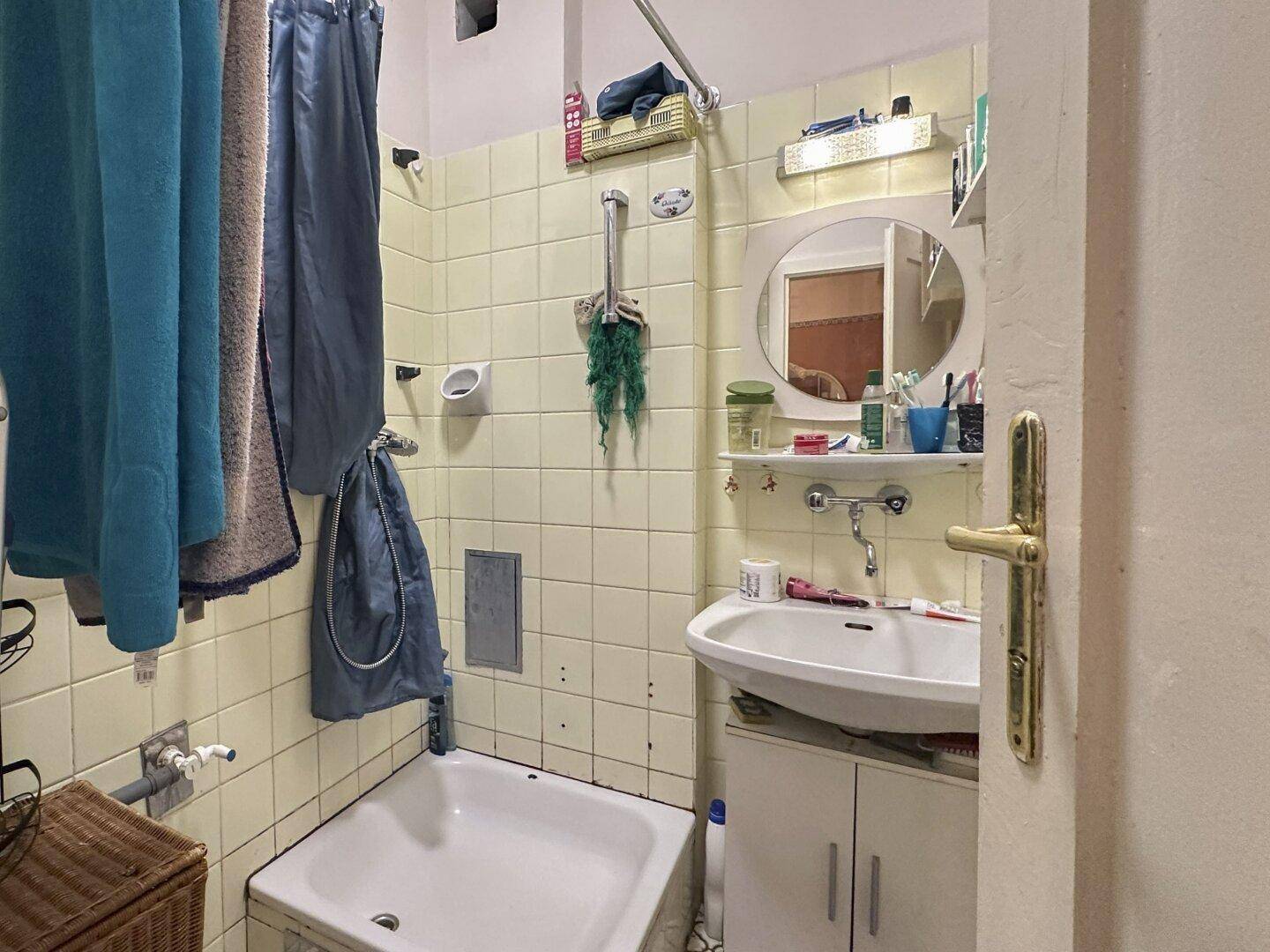Kleines Badezimmer mit Badewanne, Waschbecken und gelben Fliesen, im Originalzustand.