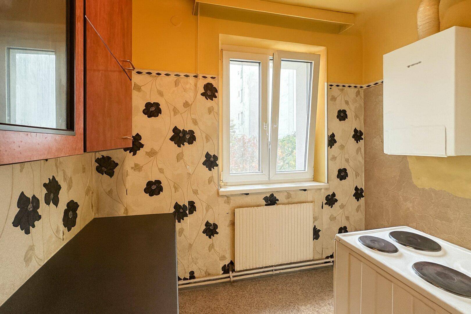 Ältere Küche mit floraler Tapete, Fenster und einfacher Ausstattung, bereit zur Modernisierung.
