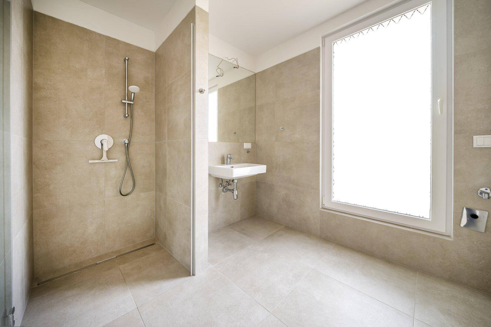 Modernes Badezimmer mit beigefarbenen Fliesen, ebenerdiger Dusche und großem Fenster.