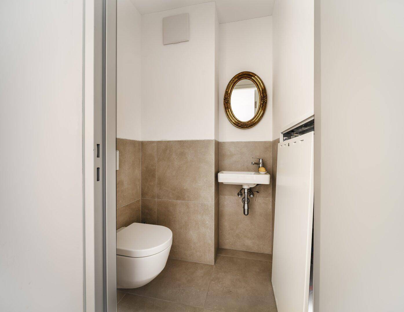 Kleines Gäste-WC mit wandhängender Toilette, Waschbecken und einem dekorativen Spiegel.