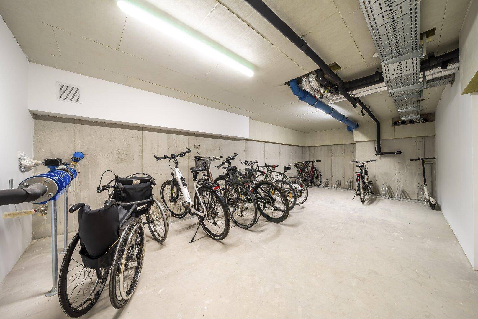 Geräumiger Fahrradraum im Untergeschoss mit mehreren Fahrrädern und einem Rollstuhl.
