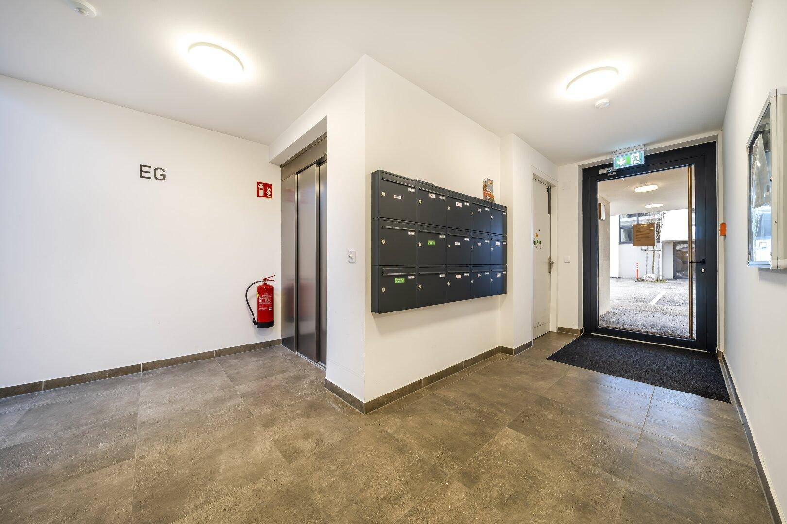 Eingangsbereich des Gebäudes mit Briefkästen, Aufzug und Fliesenboden.