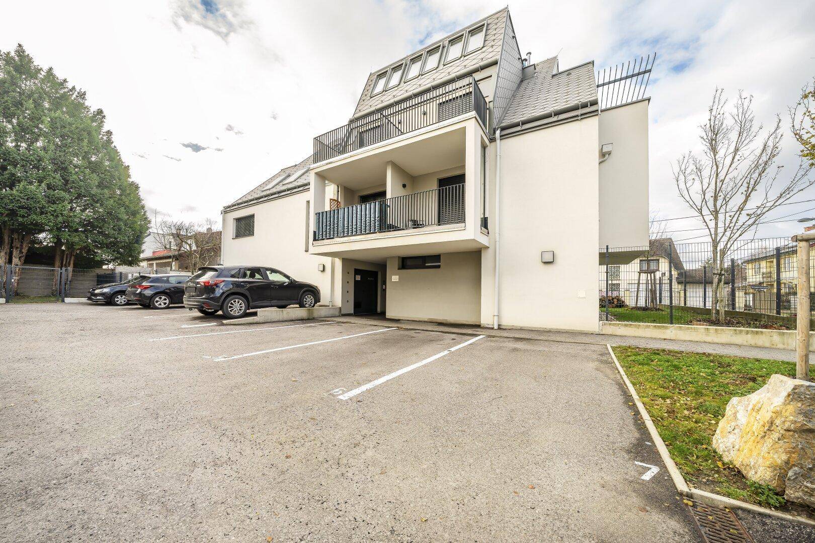 Modernes Mehrfamilienhaus mit Balkonen und Außenparkplätzen unter bewölktem Himmel.