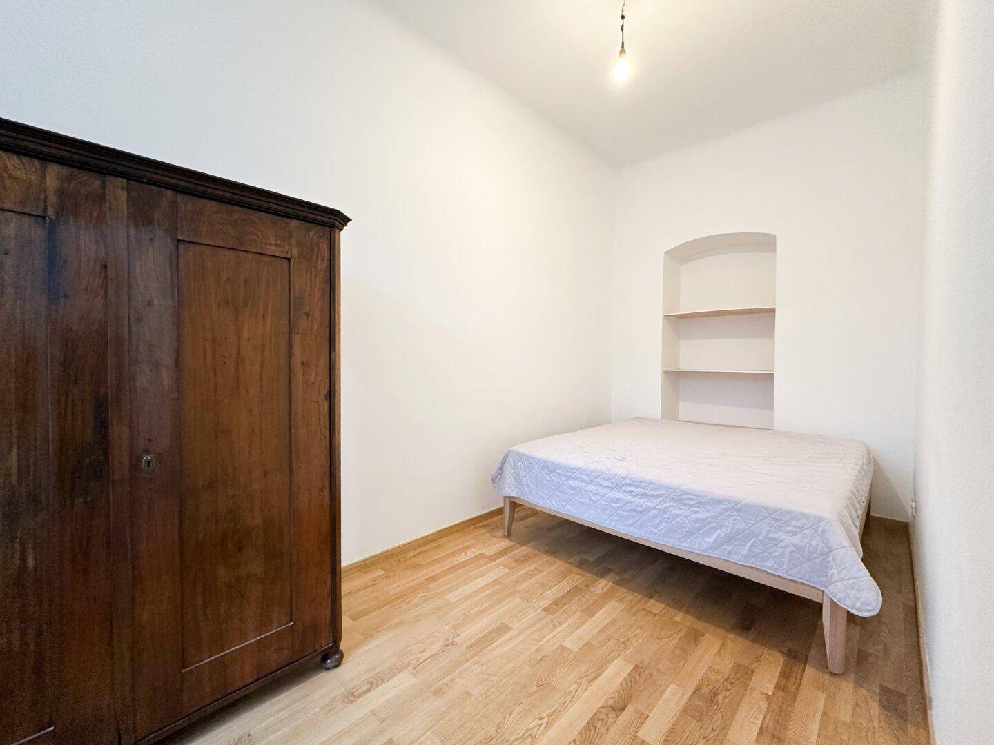 Schlafzimmer mit Holzboden, einem Bett und einem antiken Holzschrank.