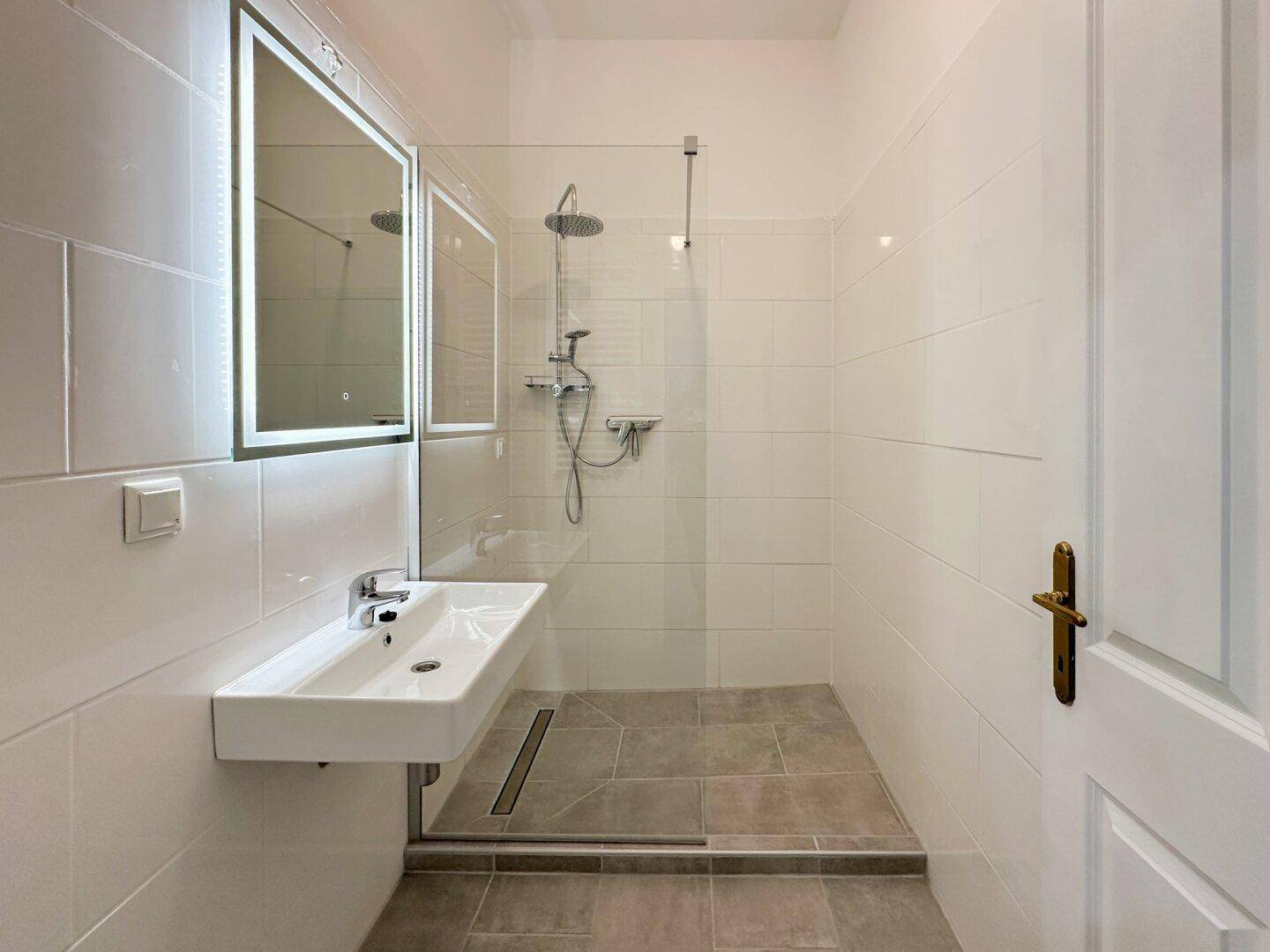 Modernes Badezimmer mit ebenerdiger Dusche, weißen Fliesen und einem Wandwaschbecken.