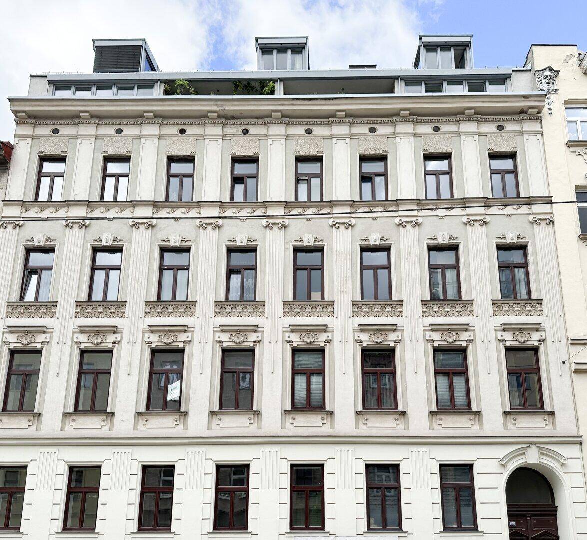 Historische Fassade eines Mehrfamilienhauses mit vielen Fenstern und Dachaufbauten.