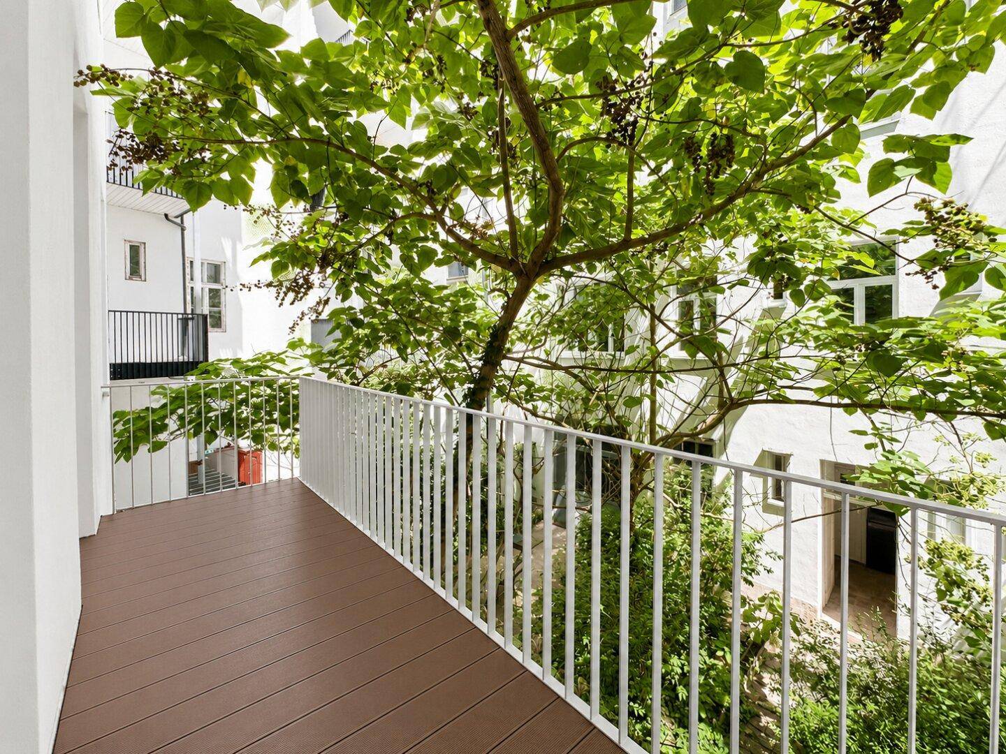 Balkon mit Blick auf einen grünen Innenhof und umliegende Gebäude, ideal zum Entspannen.