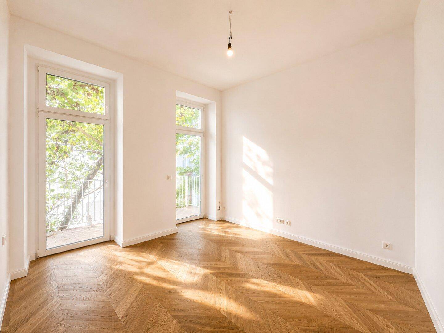 Helles Zimmer mit Fischgrätparkett und Zugang zu einem französischen Balkon, umgeben von Grün.