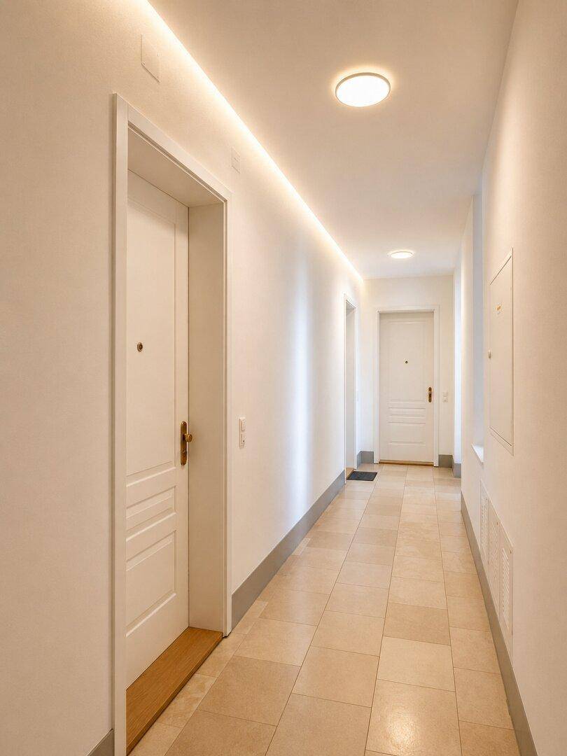 Moderner Flur mit Fliesenboden und indirekter Deckenbeleuchtung, der zu den Wohnungen führt.