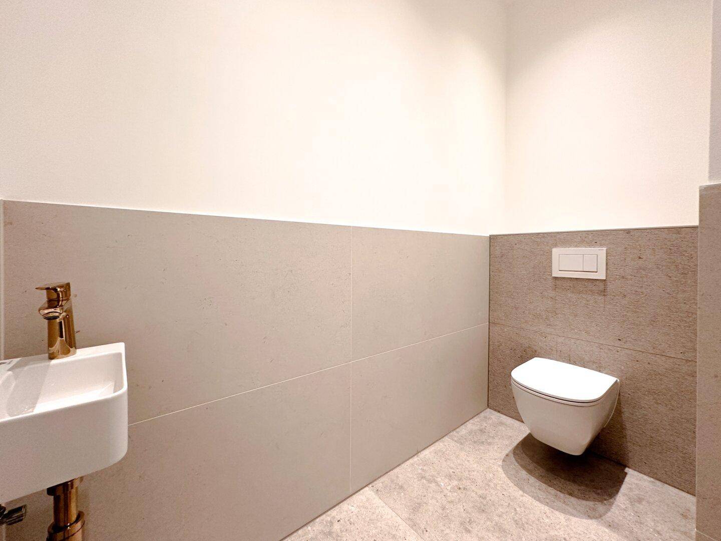 Modernes Gäste-WC mit kleinem Waschbecken und wandhängender Toilette in hellen Farbtönen.