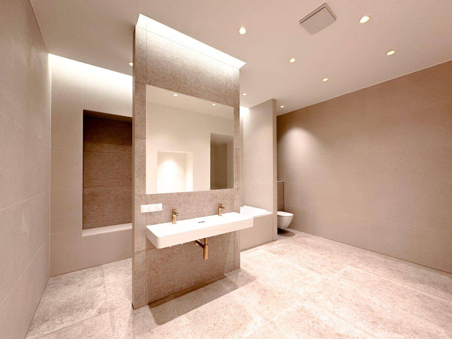 Modernes Badezimmer mit Doppelwaschbecken, großen Fliesen und integrierter Beleuchtung.