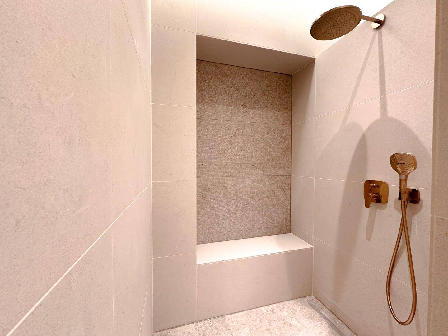 Geräumige begehbare Dusche mit Regenduschkopf und integrierter Sitzgelegenheit in modernem Design.