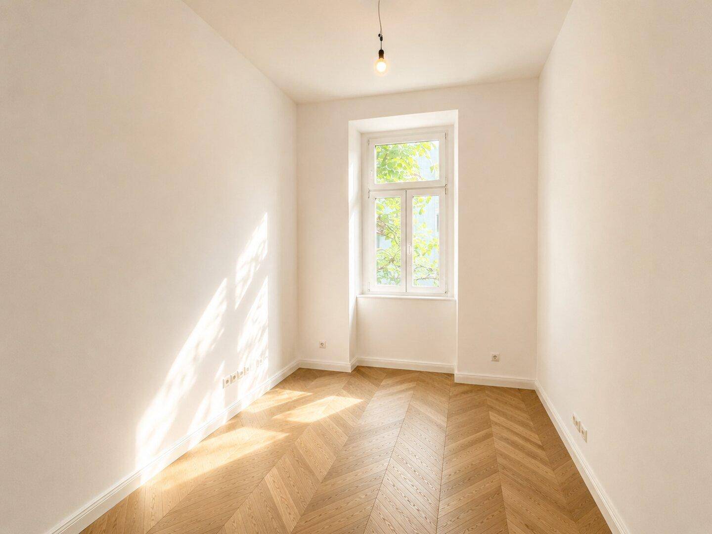 Heller Raum mit Fischgrätparkett und einem Fenster, das einen Blick ins Grüne bietet.