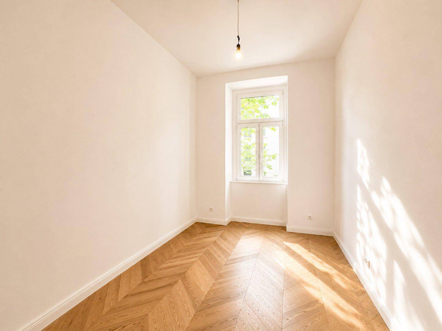 Gemütliches Zimmer mit Fischgrätparkett und einem großen Fenster, das viel Licht spendet.