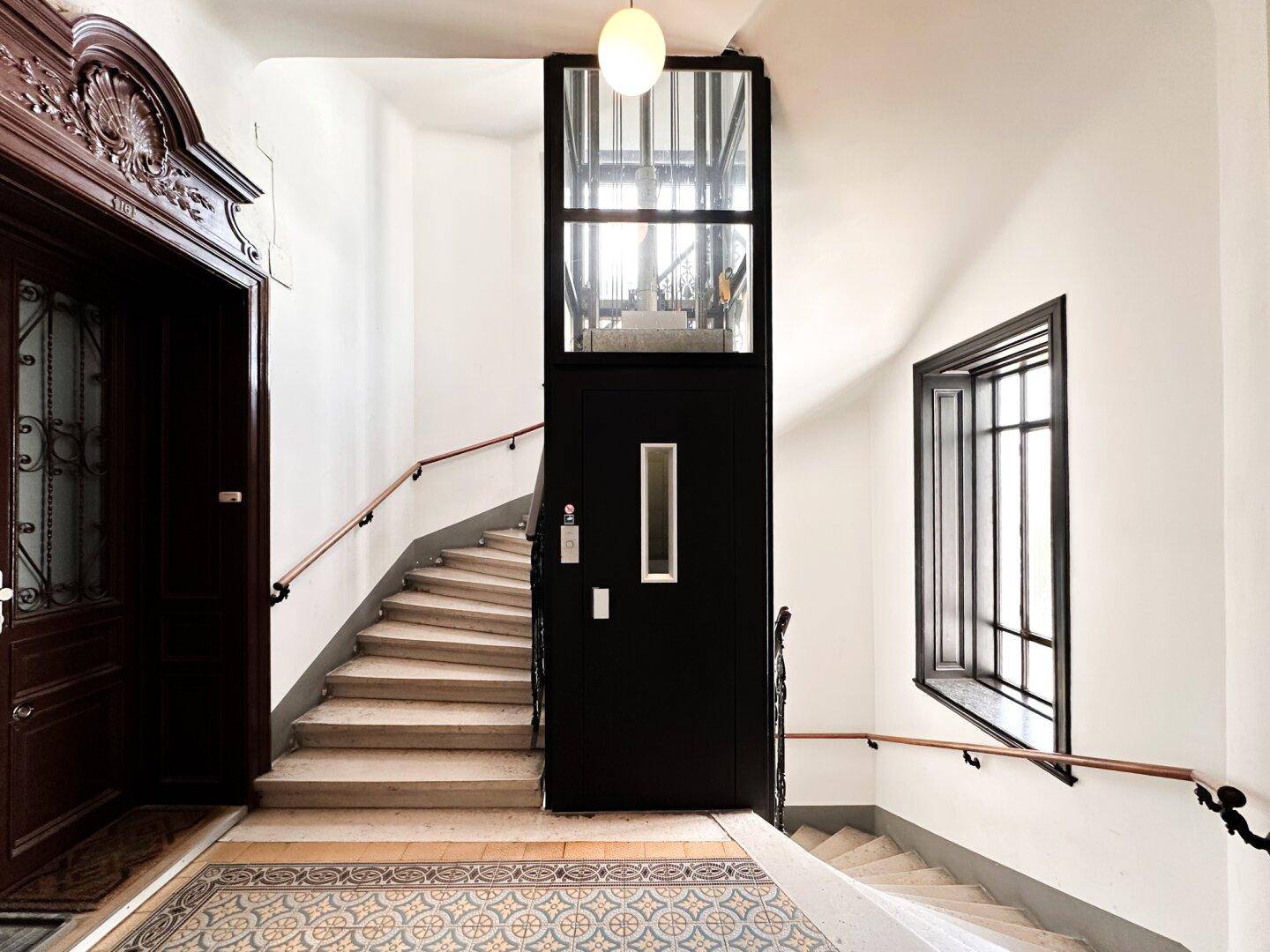 Elegantes Treppenhaus mit historischem Fliesenboden und modernem Glasaufzug für Komfort.
