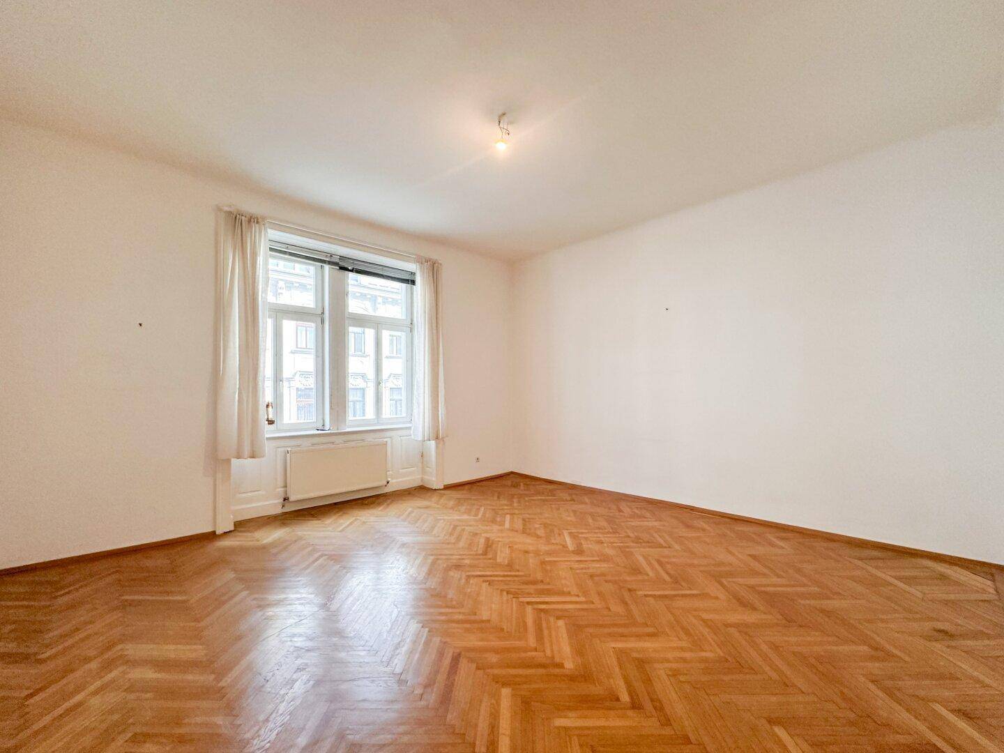 Geräumiges Zimmer mit klassischem Fischgrätparkett und viel Tageslicht durch das große Fenster.