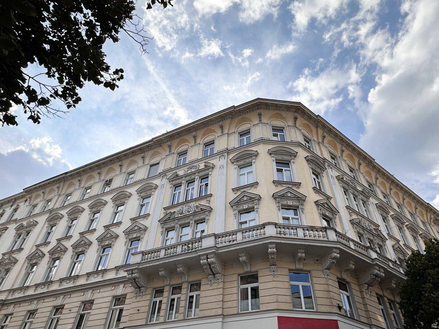 Prächtige Fassade eines Altbaus mit vielen Fenstern und dekorativen Balkonen unter bewölktem Himmel.