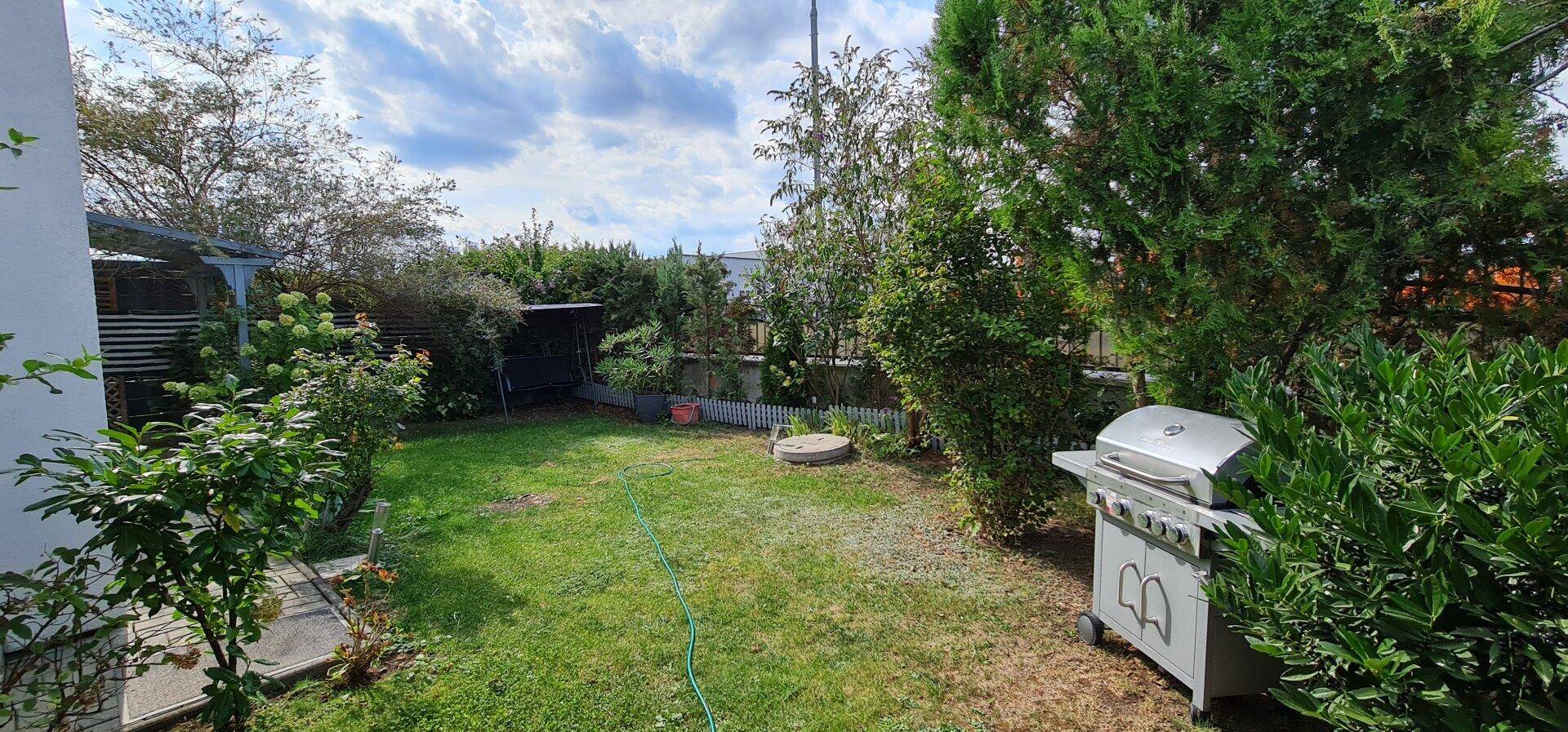 Großer Garten mit Rasenfläche, Grillbereich und üppiger Vegetation für Outdoor-Aktivitäten.