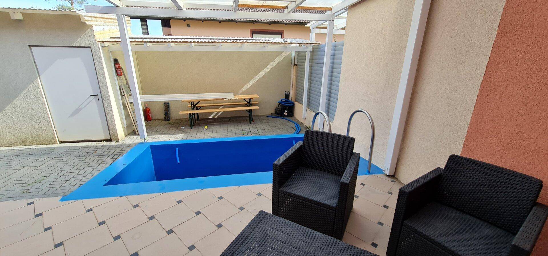 Außenbereich mit kleinem Pool, gepflasterter Terrasse und Sitzgelegenheiten unter einer Überdachung.