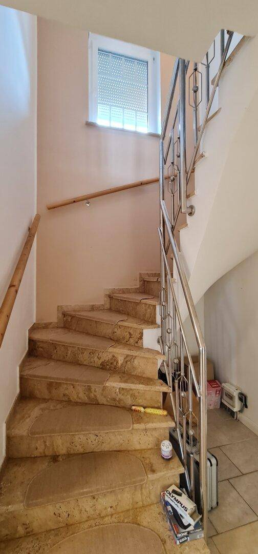 Elegante Steintreppe mit Metallgeländer und Fenster für natürliches Licht im Treppenhaus.