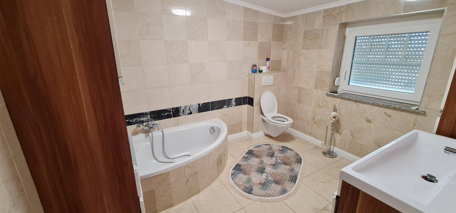 Geräumiges Badezimmer mit Badewanne, WC, Fliesenboden und Fenster für natürliche Belüftung.