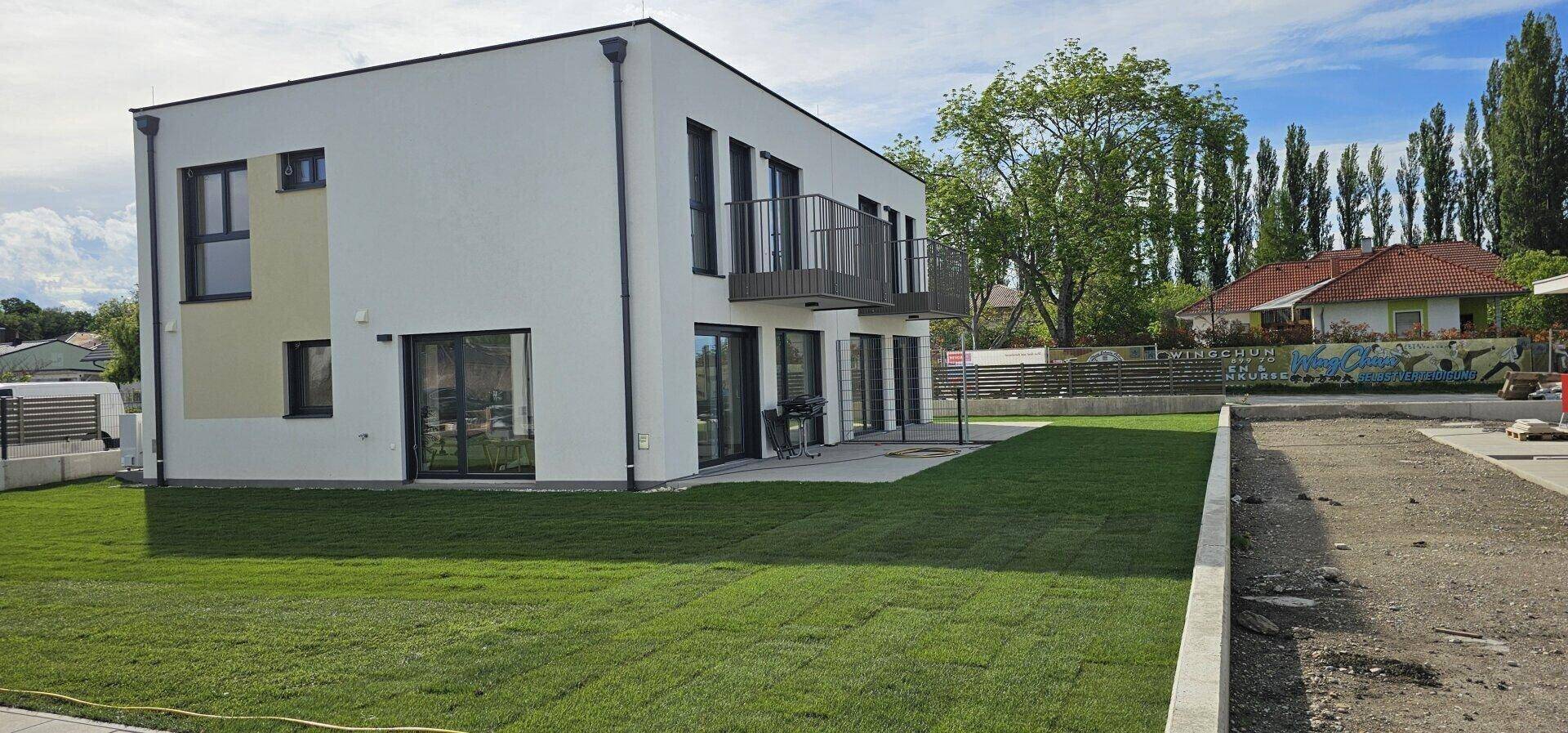Neubau-Reihenhaus mit frisch angelegtem Rasen und moderner Architektur unter blauem Himmel.