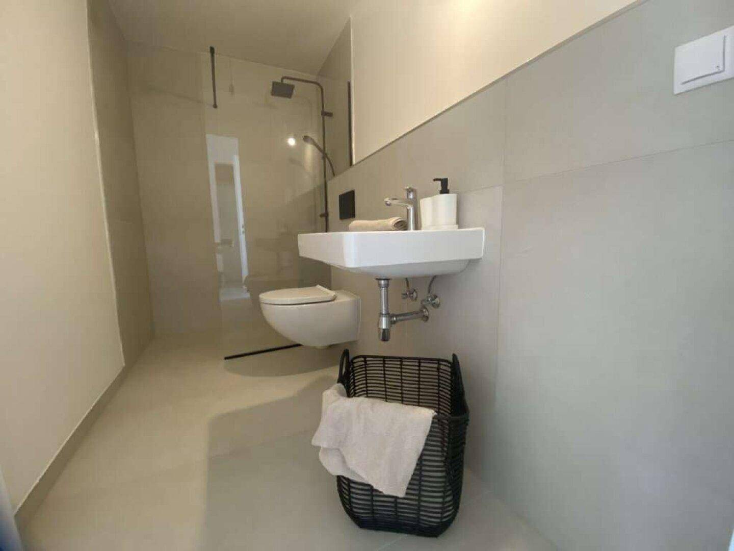 Modernes Badezimmer mit begehbarer Dusche, Wand-WC und eleganten grauen Fliesen.