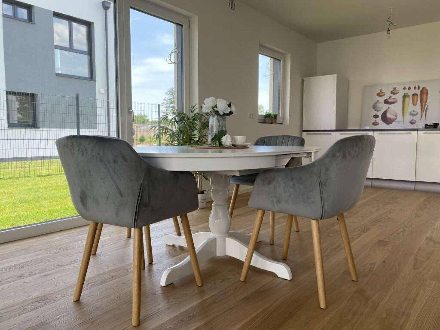 Moderner Essbereich mit rundem Tisch und Stühlen, angrenzend an eine helle Küche mit Gartenblick.