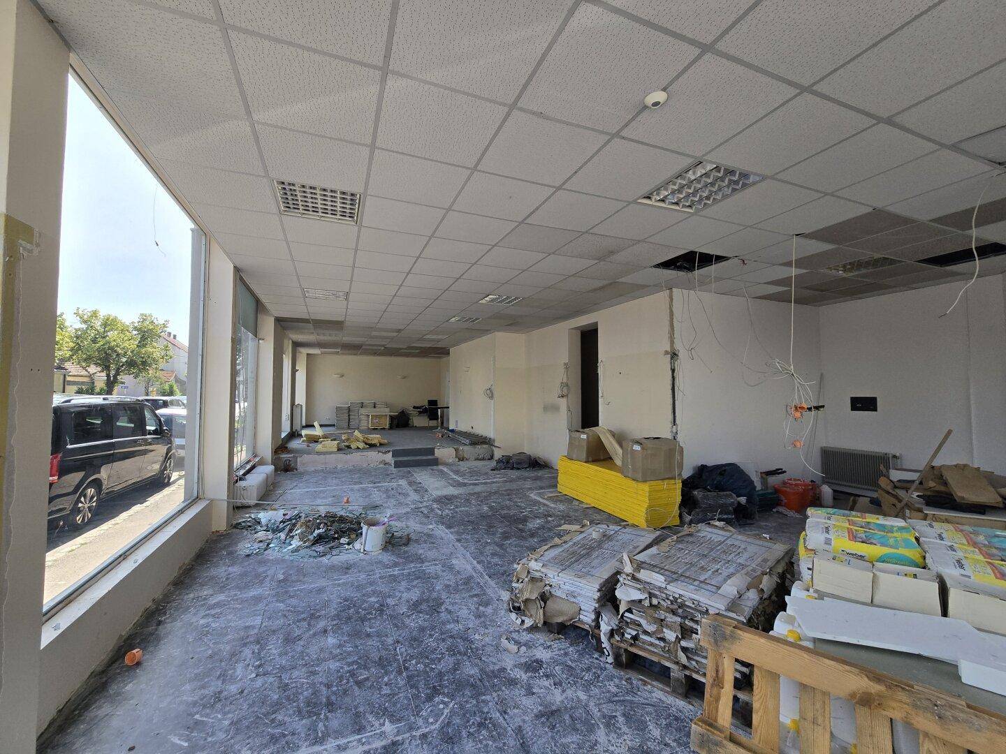 Renovierungsbedürftiger Gewerberaum mit großen Schaufenstern zur Straße und abgehängter Decke.