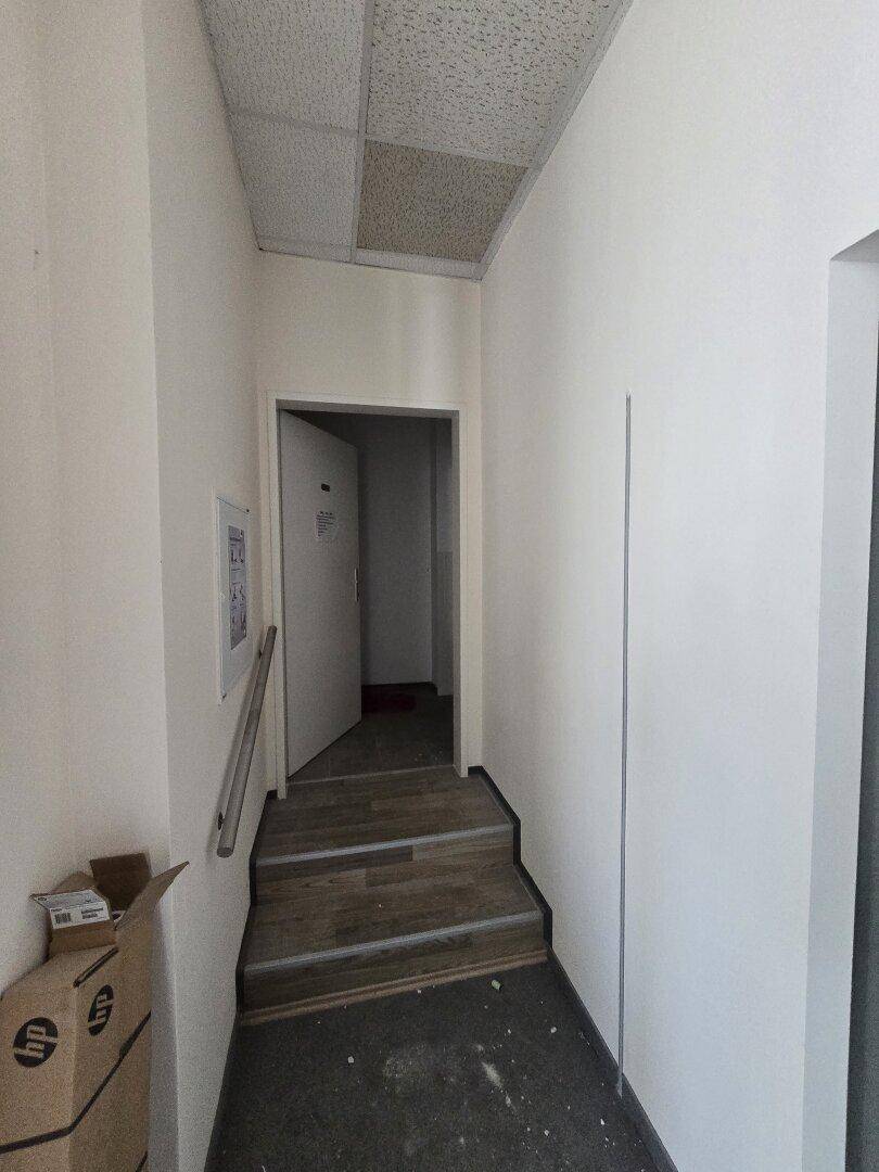 Schlichter Flur mit Treppe und abgehängter Decke, der zu weiteren Räumen führt.