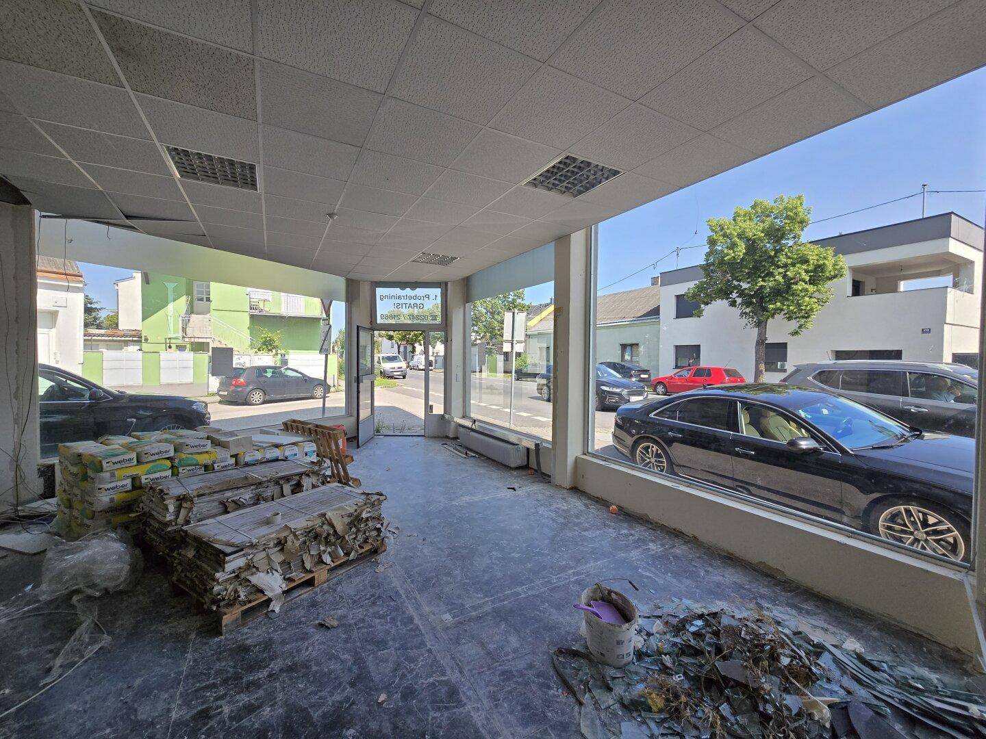 Heller Gewerberaum mit großen Fensterfronten, die einen Blick auf die Straße und parkende Autos bieten.