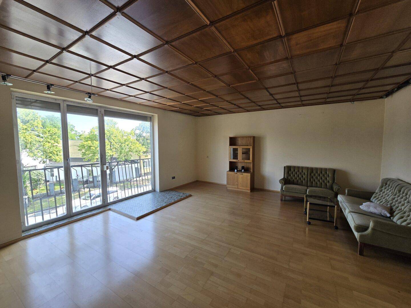 Geräumiges Wohnzimmer mit Parkettboden, Holzdecke, Balkonzugang und Vintage-Möbeln.
