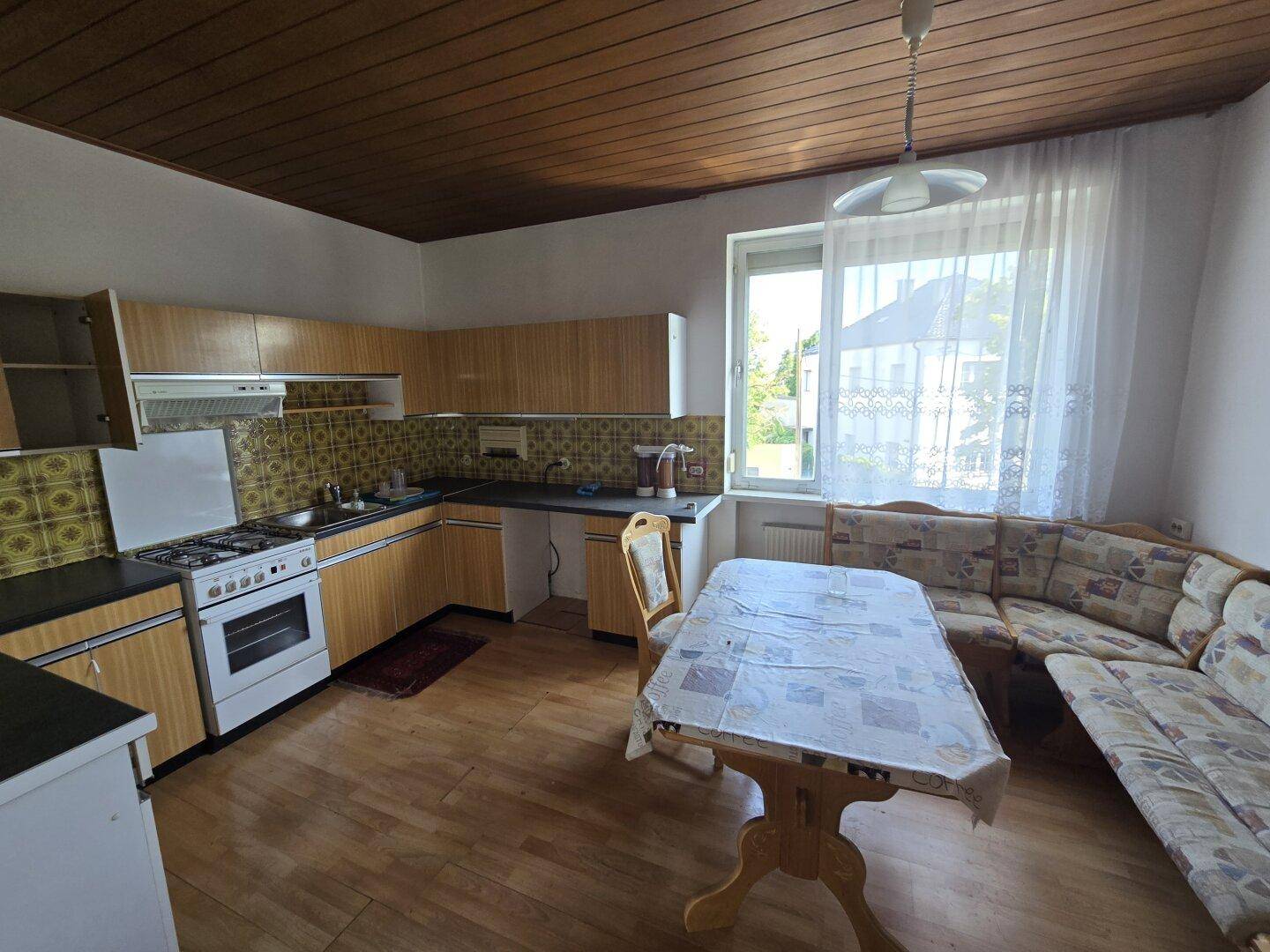 Gemütliche Wohnküche mit Holzschränken, Essbereich und Fenster, im traditionellen Stil.
