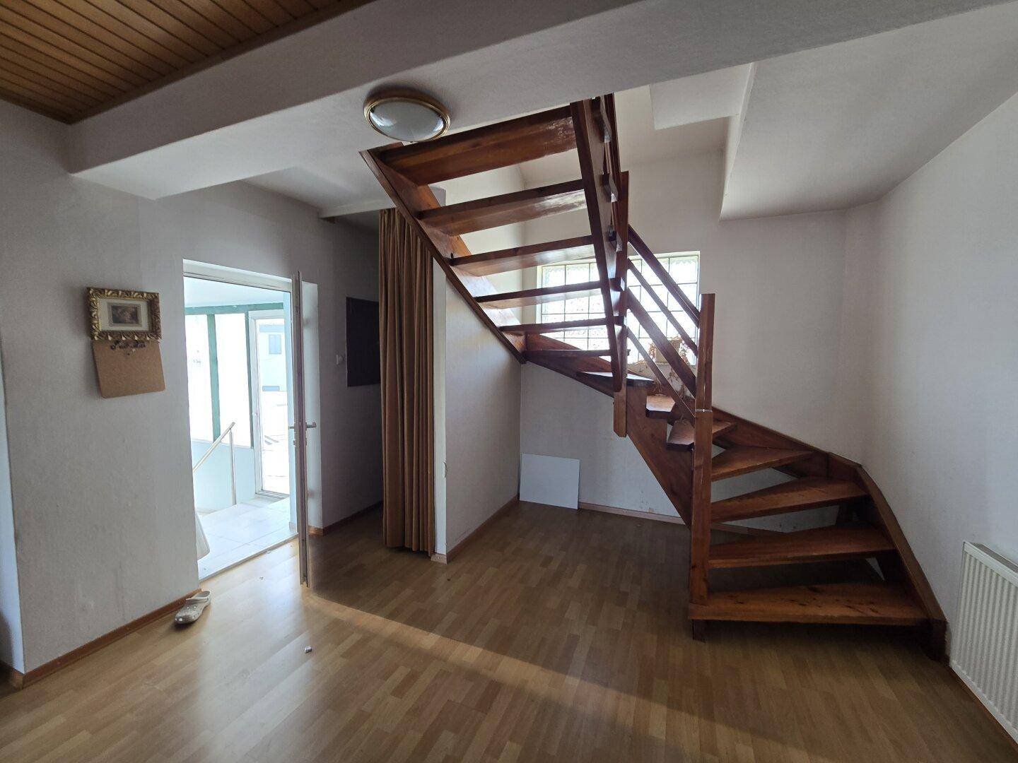 Heller Eingangsbereich mit einer Holztreppe und einer Holzpaneeldecke, die zum Obergeschoss führt.