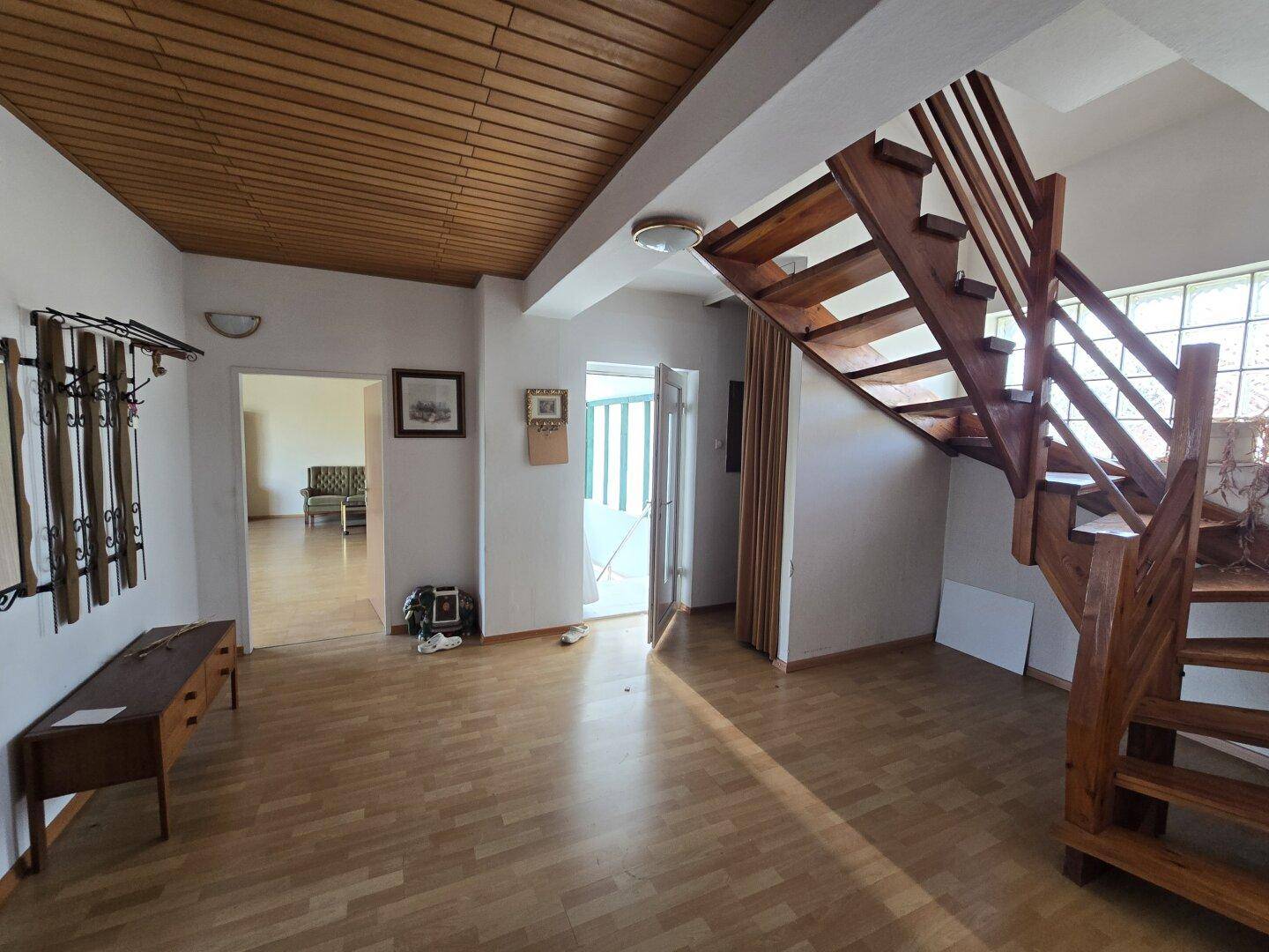 Geräumiger Flur mit Holztreppe, Garderobe und Holzdecke, der verschiedene Bereiche verbindet.