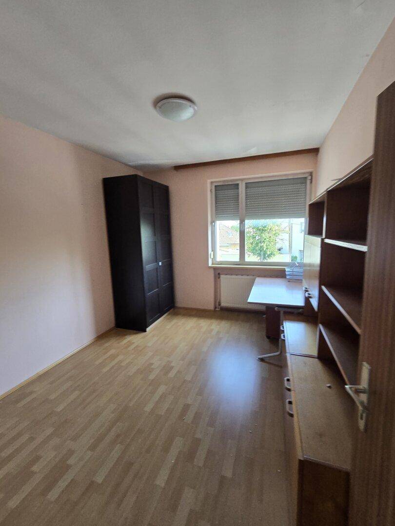 Helles Schlafzimmer oder Büro mit Laminatboden, Kleiderschrank und Schreibtisch am Fenster.