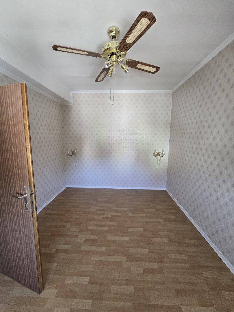 Leerer Raum mit gemusterter Tapete, Laminatboden und Deckenventilator, bereit zur Gestaltung.