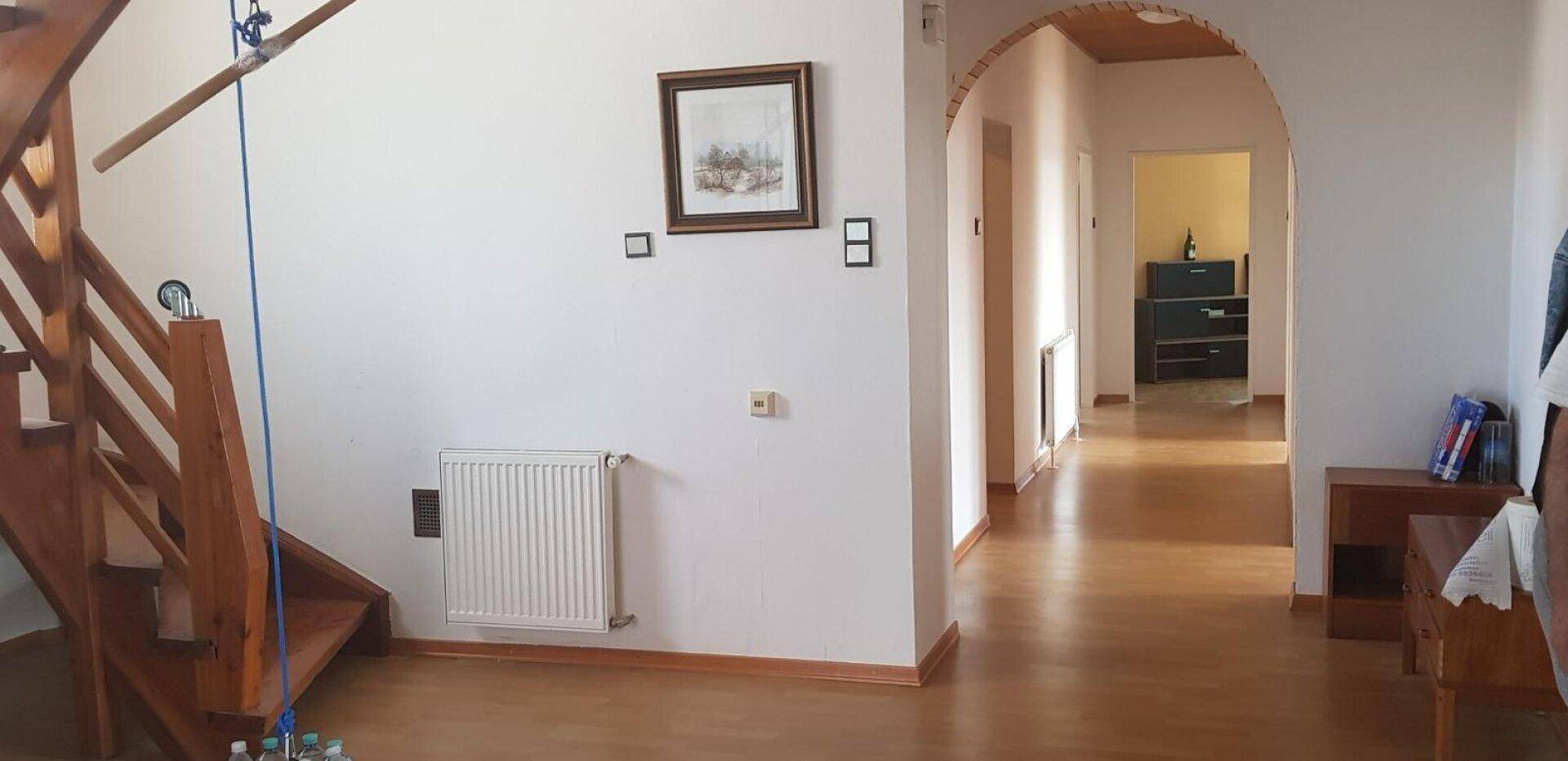 Geräumiger Flur mit Holztreppe, Heizkörper und einem dekorativen Rundbogen.