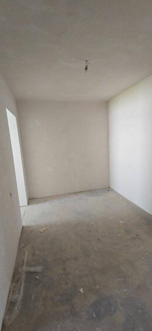 Leeres Zimmer in Renovierung mit rohen Wänden und Betonboden, bereit für den Ausbau.