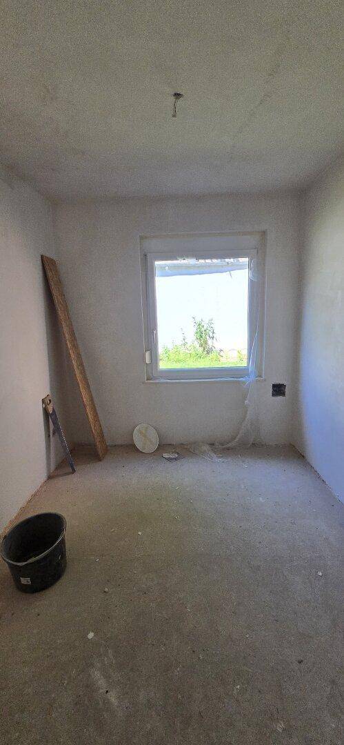 Leeres Zimmer in Renovierung mit Betonboden und einem Fenster, das Tageslicht hereinlässt.