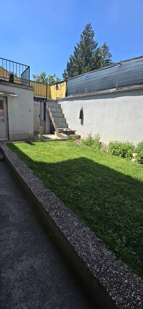 Garten mit Rasenfläche, Treppe zum oberen Bereich und einer hohen Mauer.
