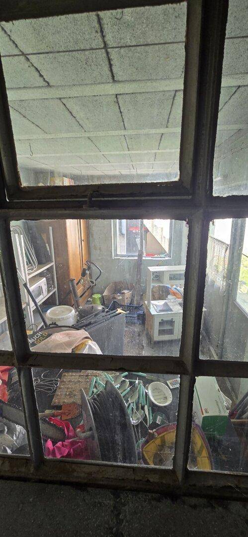 Blick durch ein schmutziges Fenster in einen unaufgeräumten Raum mit verschiedenen Gegenständen.