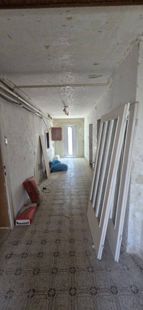Langer Flur in einem renovierungsbedürftigen Zustand mit alten Fliesen und Baumaterialien.